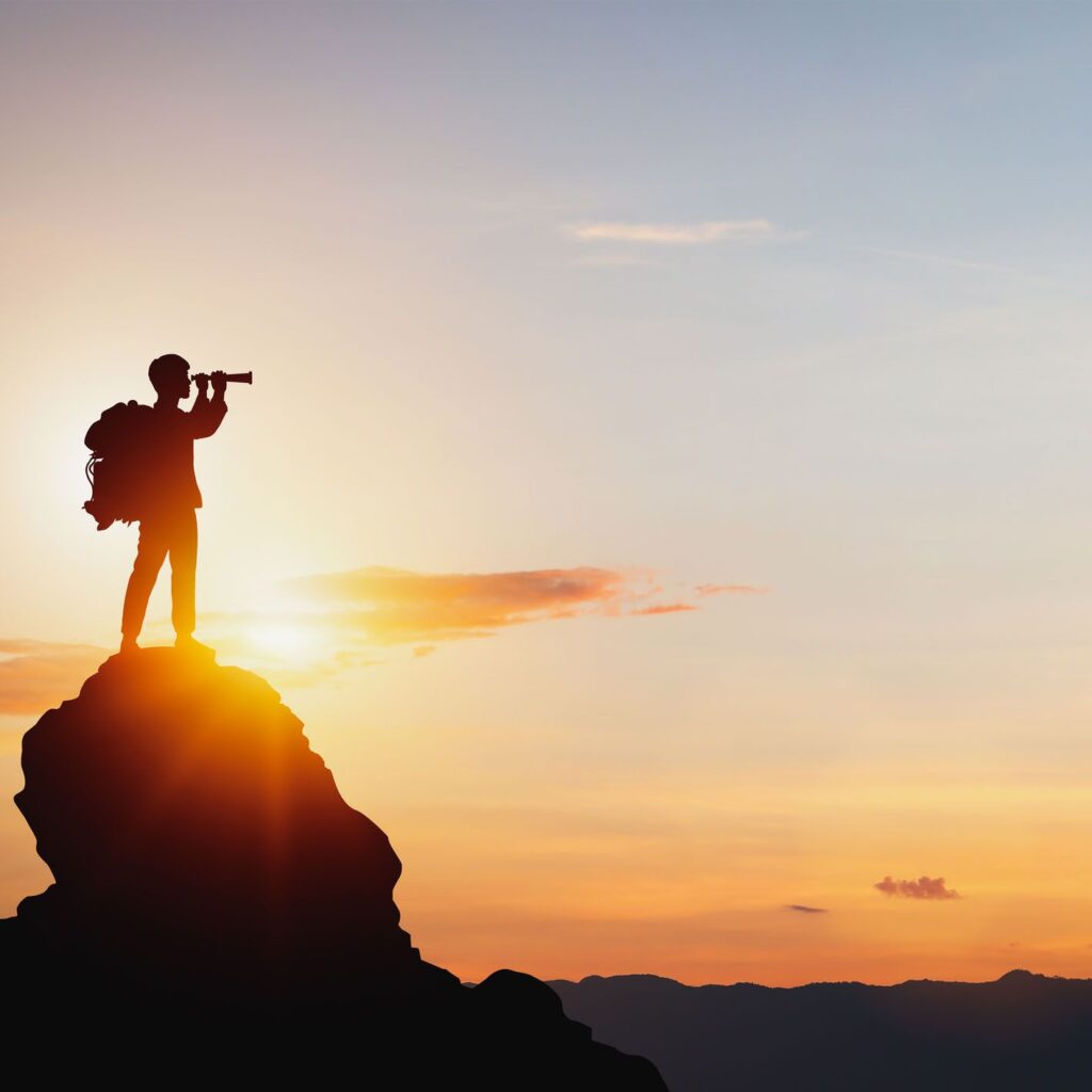 A person with a backpack standing on a mountain peak holding a spyglass