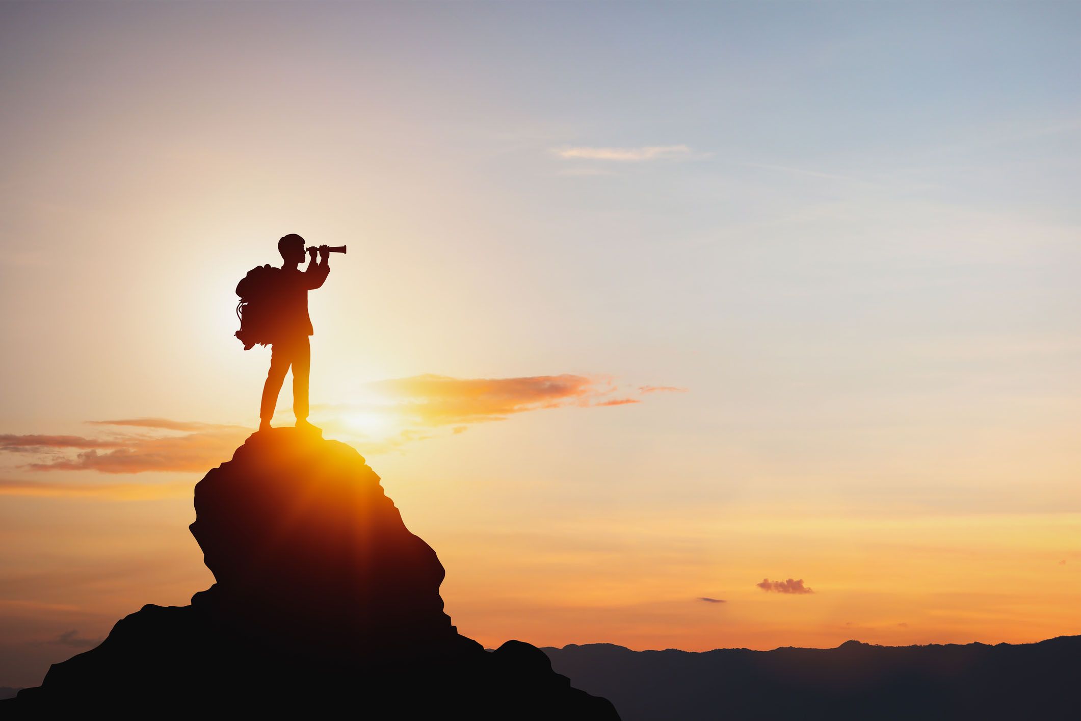 A person with a backpack standing on a mountain peak holding a spyglass